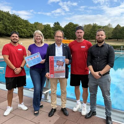 Vier M&auml;nner und eine Frau stehen vor dem Schwimmbecken. Sie machen auf eine Kampagne zum Schutz der Besucher aufmerksam. 